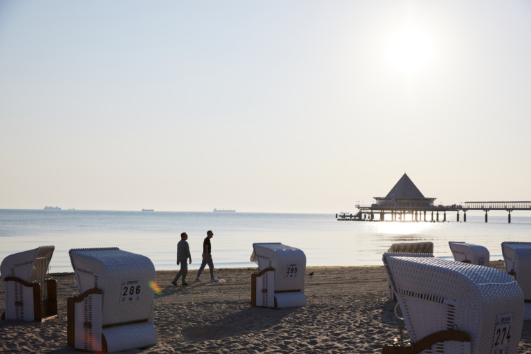 Strandkörbe und Spaziergänger am Ostseestrand von Usedom – Sonnenaufgang mit Blick auf die berühmte Seebrücke.