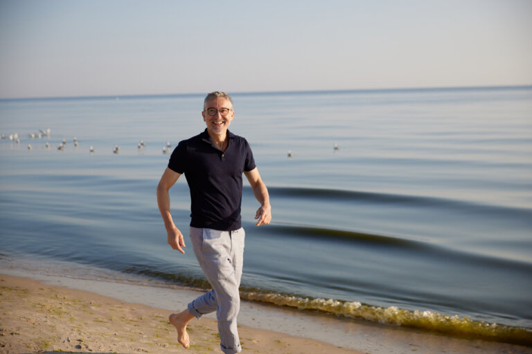 Glücklicher Mann läuft barfuß am Ostseestrand auf Usedom – aktiver Urlaub mit Meerblick, Sonne und Erholung.