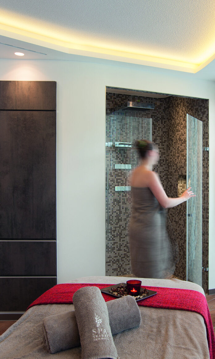 Eine Frau im Bademantel nutzt den Wellnessbereich eines Wellnesshotels im Schwarzwald, im Vordergrund ist ein Massagetisch mit gerollten Handtüchern darauf.