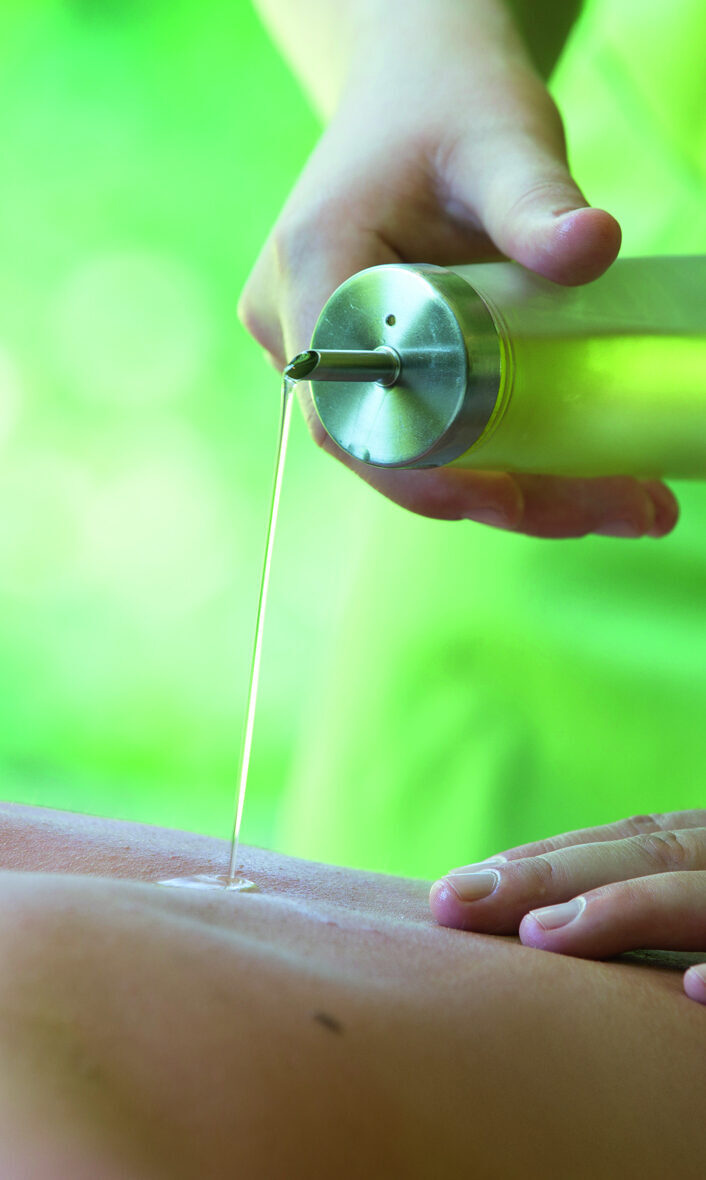 Eine Person gießt Massageöl auf den Rücken einer liegenden Person, die Massage in einem Wellnesshotel erhält.