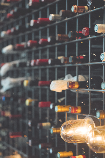 Ein Weinregal mit mehreren Flaschen in verschiedenen Farben und Formen, einige Flaschen sind teilweise sichtbar, darunter Glühbirnen als Dekoration.