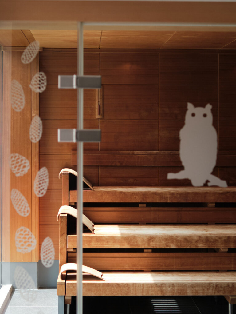 Eine Sauna mit Holzbänken, deren Glastür mit Eulenmotiv verziert ist.