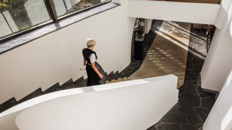 Eine Frau geht eine Treppe in einem hellen modernen Hotelflur mit großen Fenstern hinunter.
