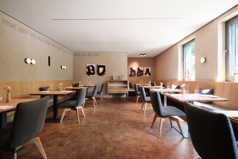 Ein Restaurantbereich mit Holztischen, grauen Stühlen und modernen Wanddekorationen.