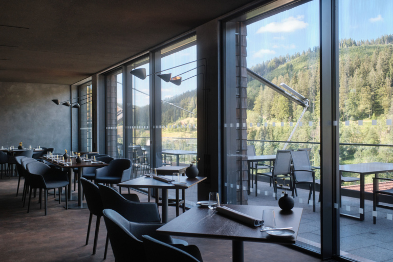 Innenansicht eines Gourmet Restaurants im Schwarzwald mit eleganten Tischen und Stühlen. Große Fenster bieten Blick auf die bewaldete Landschaft.