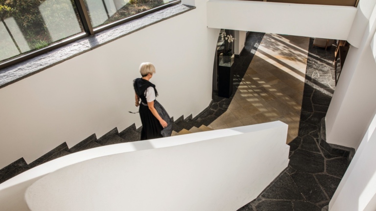 Eine Frau geht eine Treppe in einem hellen modernen Hotelflur mit großen Fenstern hinunter.