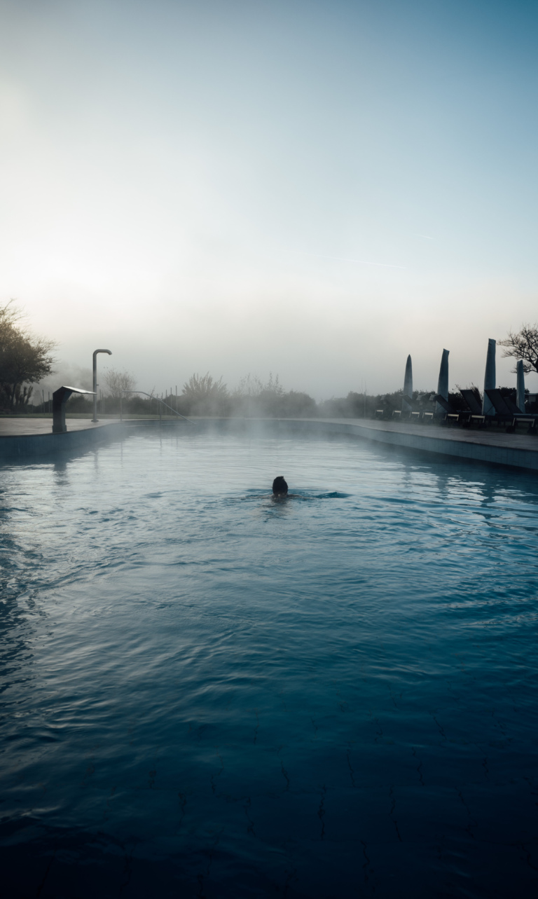 Schwimmer im beheizten Außenpool des Hotel Traube Tonbach bei Morgennebel, wo ruhige und entspannte Atmosphäre herrst.
