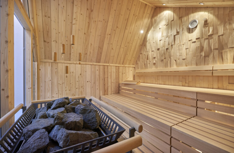Eine helle Klangsauna mit Holzbänken und Saunaofen voller Steine im Spa Bereich eines Luxushotels im Schwarzwalt.