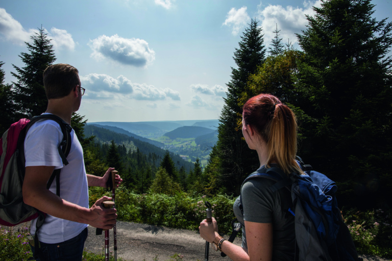 Zwei Wanderer mit Rucksäcken genießen den Ausblick über bewaldete Täler und Berge im Schwarzwald.