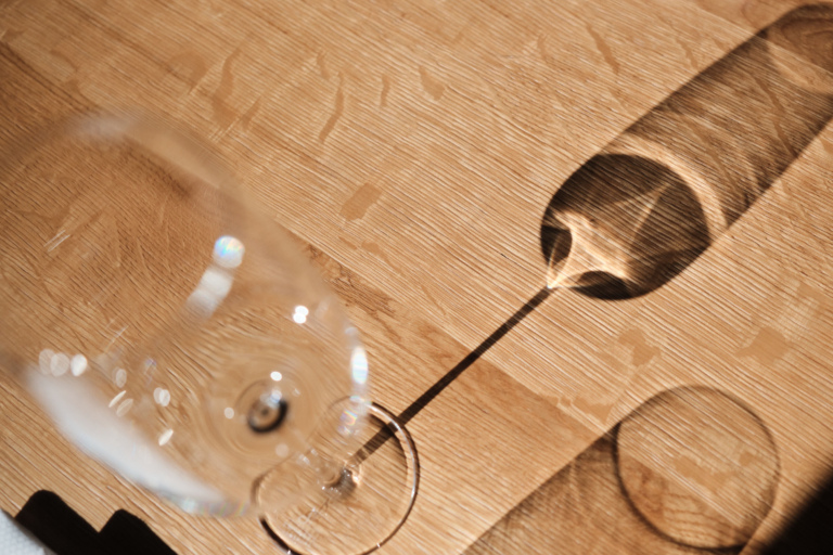 Weinglas mit elegantem Schattenspiel auf Holztisch – stilvolles Fine Dining Detail im Luxushotel Traube Tonbach Schwarzwald.