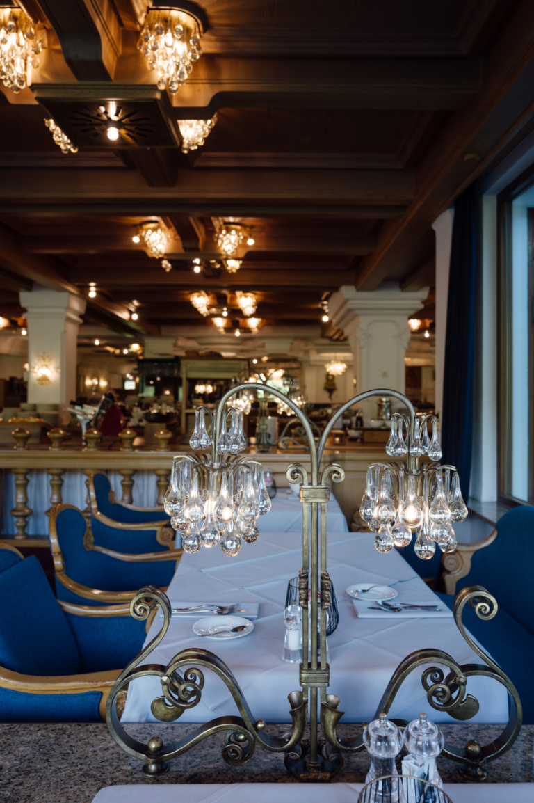 Ein Gourmet Restaurant mit gedeckten Tischen, blauen Stühlen und einer Kronleuchterbeleuchtung.