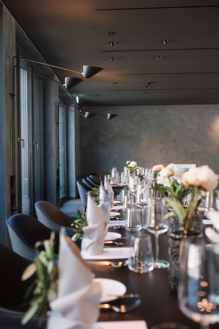 Elegante Restaurant-Tische mit modernen dunkelblauen Stühlen, weißen Tischdecken, Gläsern, Besteck und Blumenarrangements.