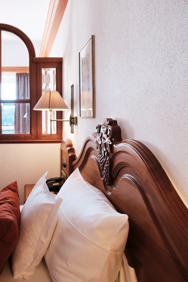 Ein helles Hotelzimmer mit einem Holzbettrahmen, Kissen und einer Nachttischlampe.