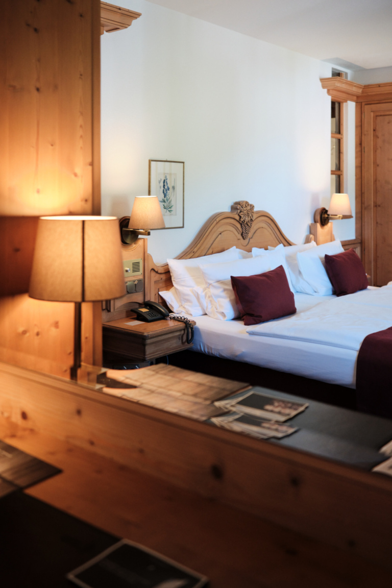 Ein einladendes Hotelzimmer mit einem Doppelbett, Nachttischen, Lampen und Holzmöbeln. Das Licht ist warm.
