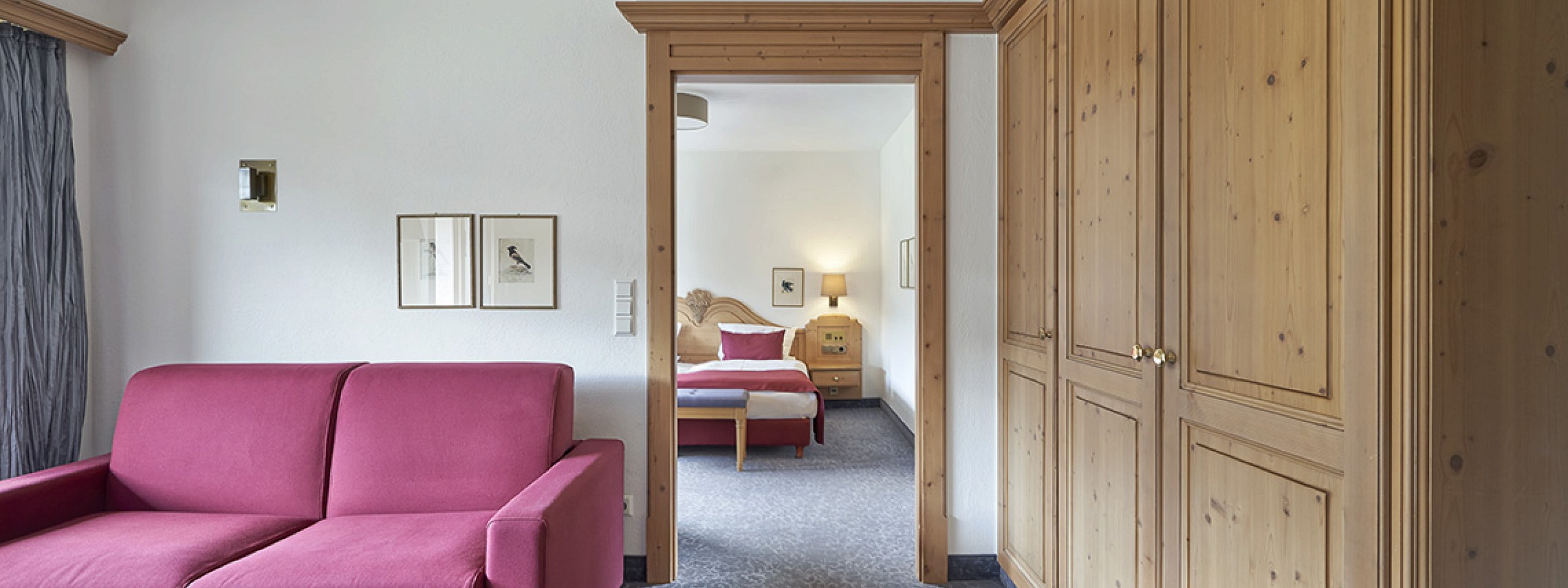 Blick in eines der Hotelzimmer im Schwarzwald mit rotem Sofa und Bett im Hintergrund.