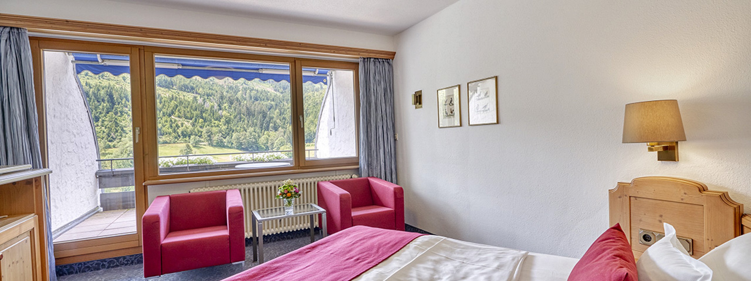 Hotelzimmer im Schwarzwald mit großem Bett und zwei roten Sesseln vor großem Fenster.