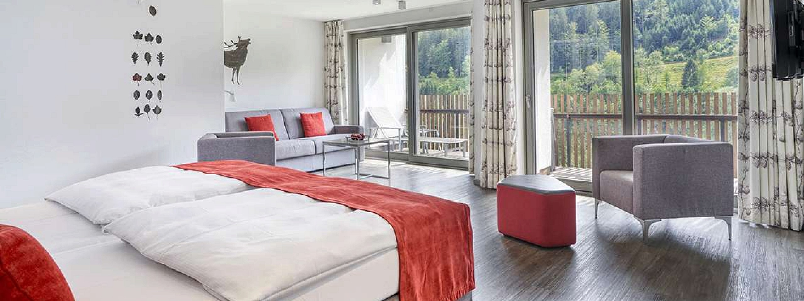 Bett mit zwei gepolsterten Stühlen sowie einem Schreibtischstuhl im Hotelzimmer im Schwarzwald.