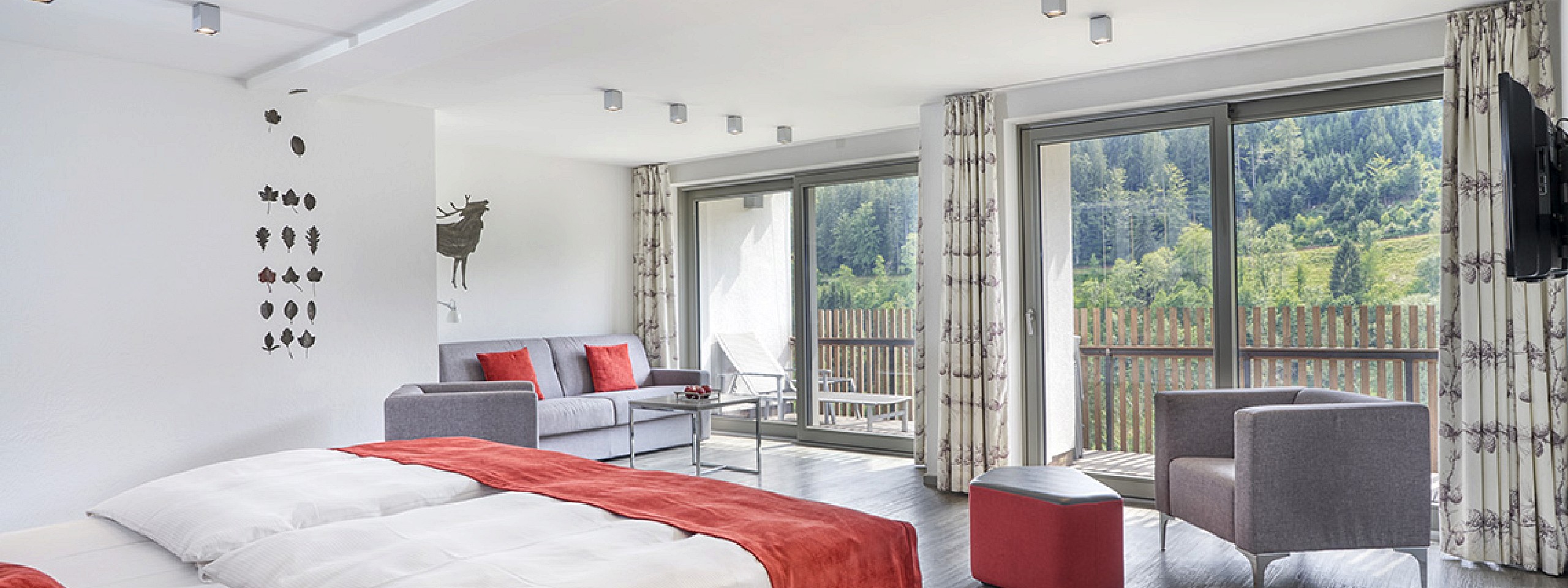 Bett mit zwei gepolsterten Stühlen sowie einem Schreibtischstuhl im Hotelzimmer im Schwarzwald.