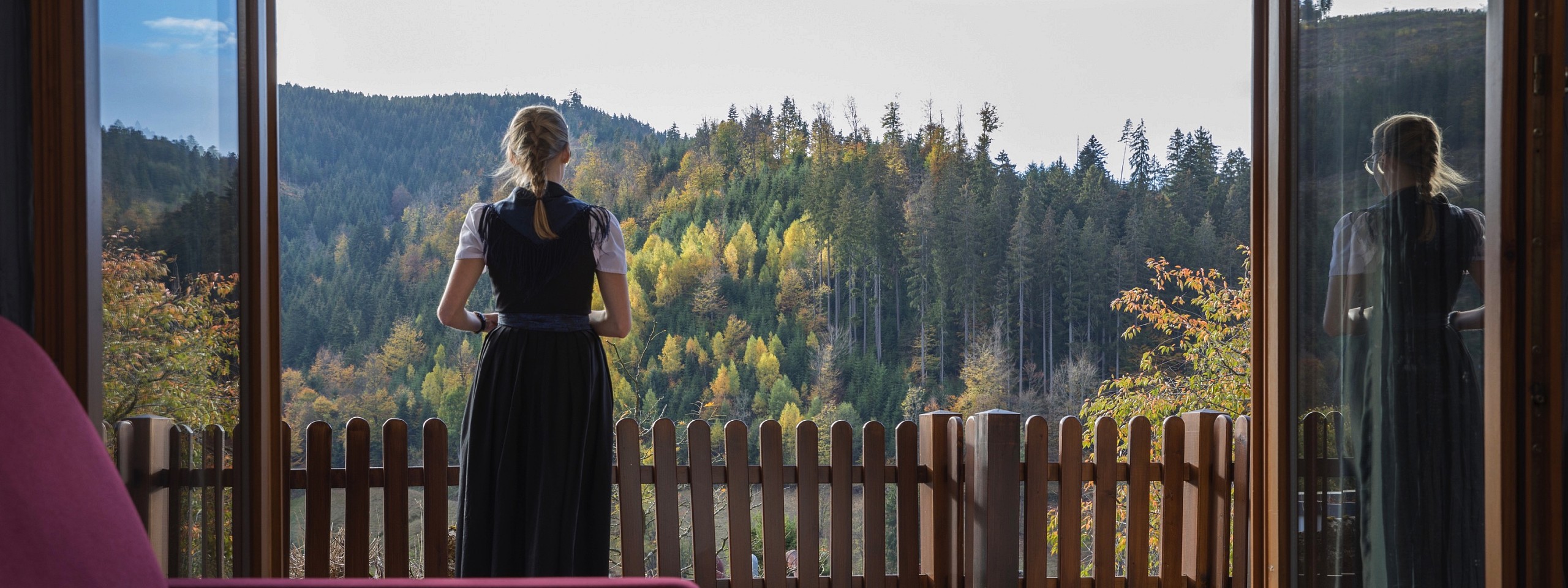 Eine junge Frau steht auf dem Balkon eines Hotelzimmers im Schwarzwald.