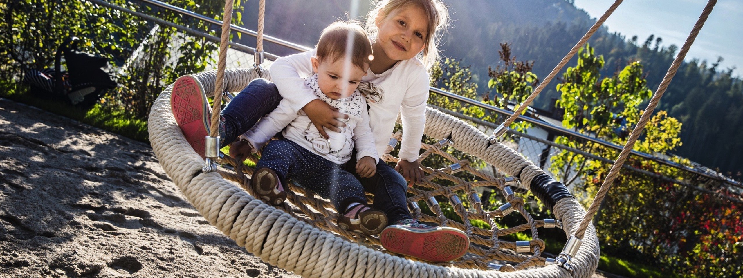 Ein junges Mädchen und ein Baby auf einer Hängeschaukel im Familienhotel im Schwarzwald.