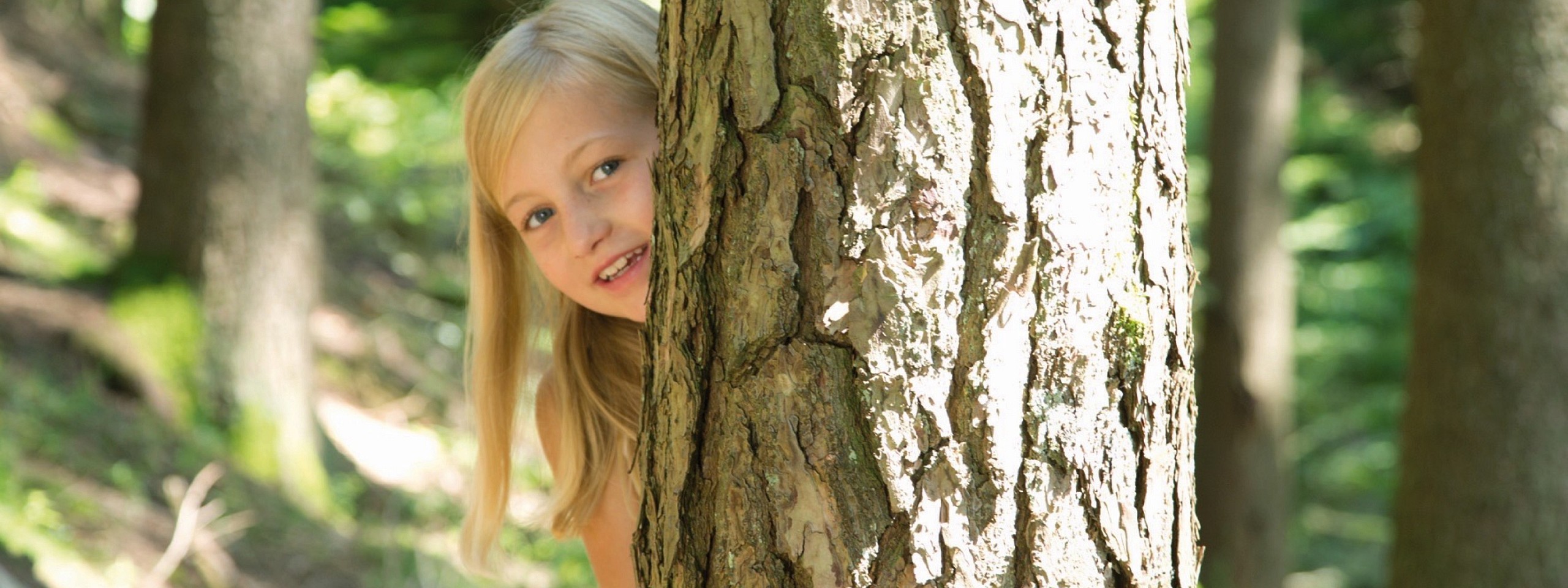Ein Mädchen guckt bei ihrem Aufenthalt in einem Hotelzimmer im Schwarzwald hinter einem Baum hervor.