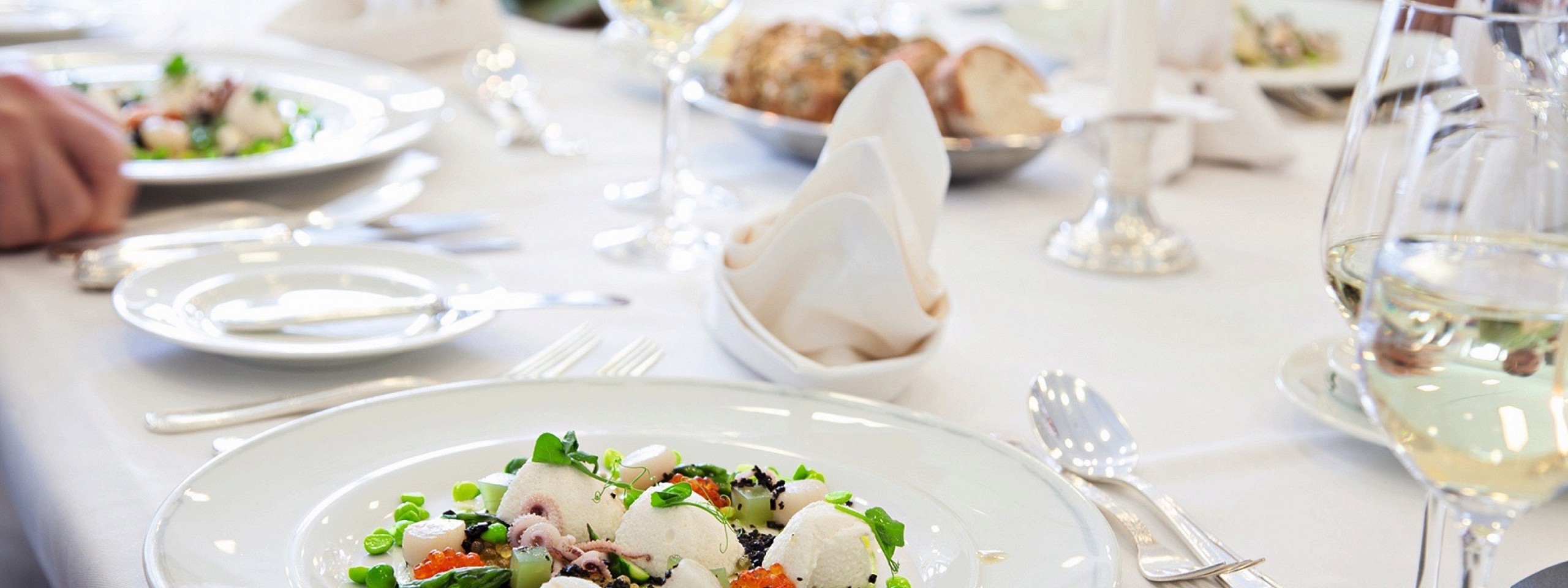 Weiß gedeckter Tisch mit Fischgerichten und Brot serviert im Restaurant in Baiersbronn.